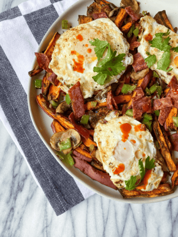 Loaded Breakfast fries on a plate with sweet potatoes, veggies, eggs, and bacon