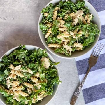 kale caesar pasta salad in two bowls with a fork
