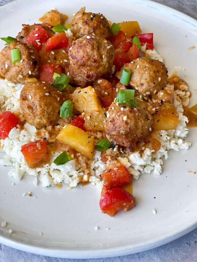 Sweet and Sour Meatballs on a plate with red peppers, pineapple chunks and green onions
