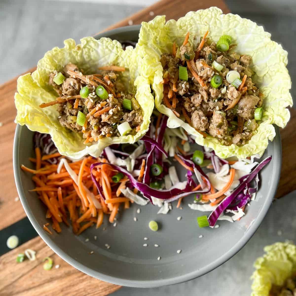Pork Lettuce Wraps on a plate with cabbage and shredded carrots