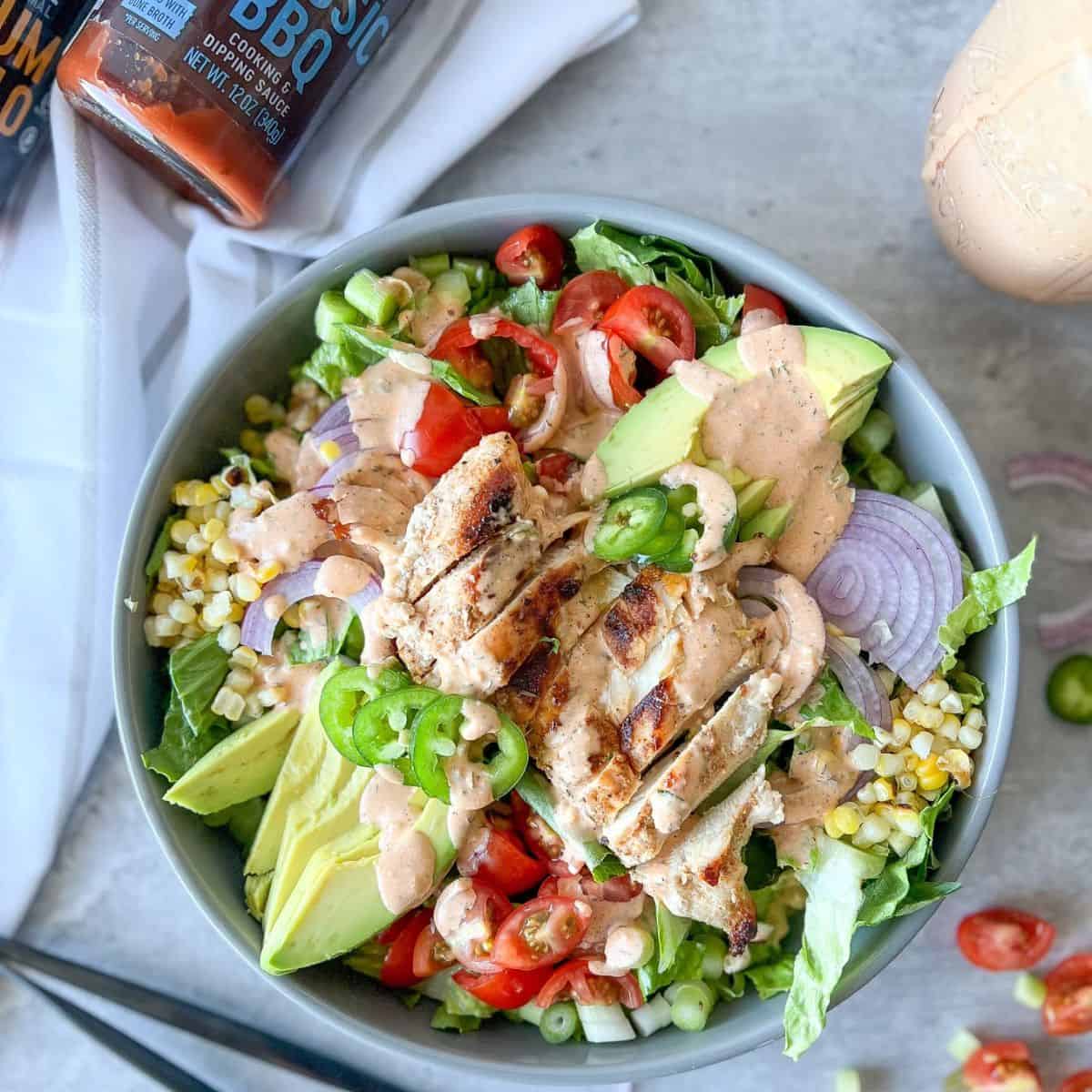 southwest bbq chicken salad in a bowl with veggies and spicy bbq ranch dressing, buffalo sauce and bbq sauce.
