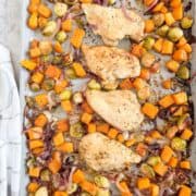 Roasted chicken breasts with sweet potatoes, Brussels sprouts, and caramelized onions on a baking sheet.
